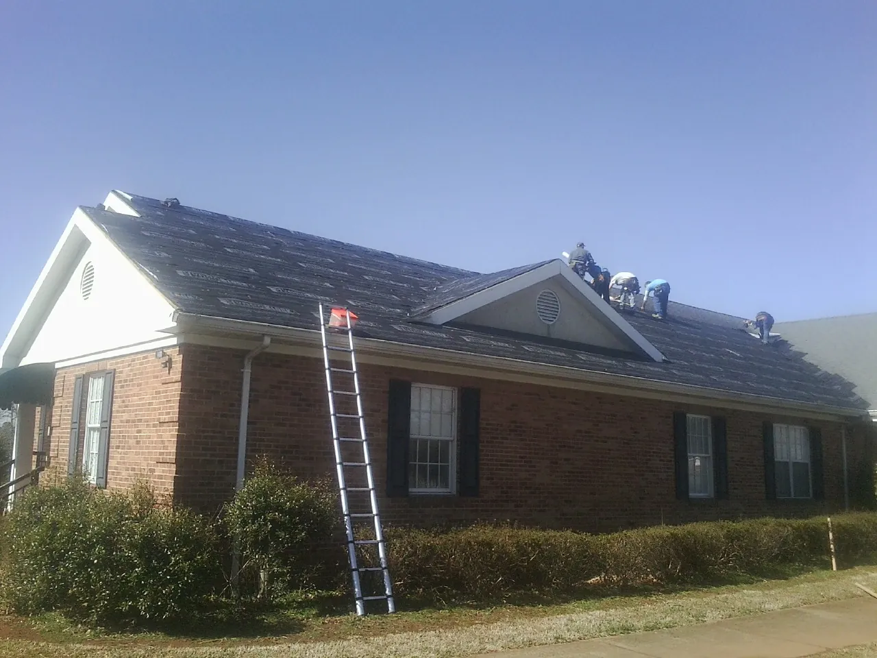 Crew tearing shingles off a brick ranch roof with a ladder set — Metal Roof Repair work by our crew in Trappe