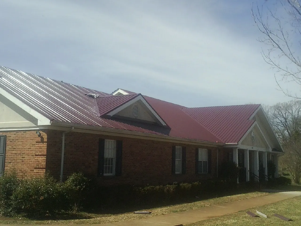 Red metal roof with gabled entries on a long brick building, from a Hail Damage Roof Repair job in Trappe