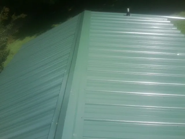 New green metal panels meeting at the ridge of a roof — Flat Roof Repair work by our crew in Trappe