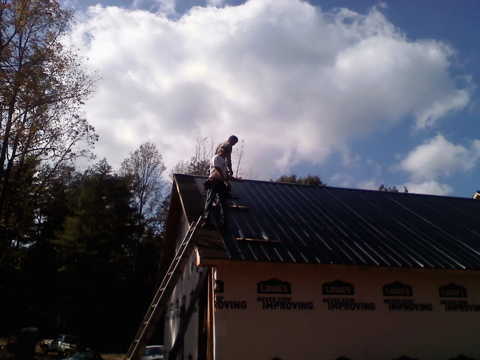 Roofer fastening dark metal panels high against a cloudy sky, from a Roof Inspection job in Trappe