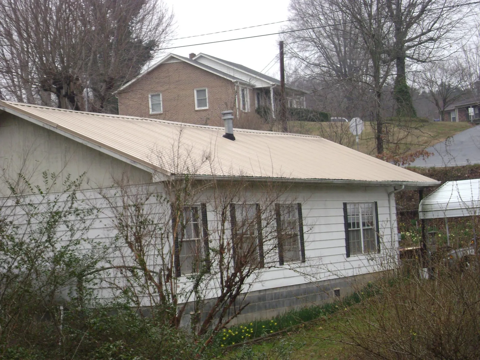 Tan metal roof on a white sided house set into a hillside — Commercial Roofing by Roofing Brothers in Trappe